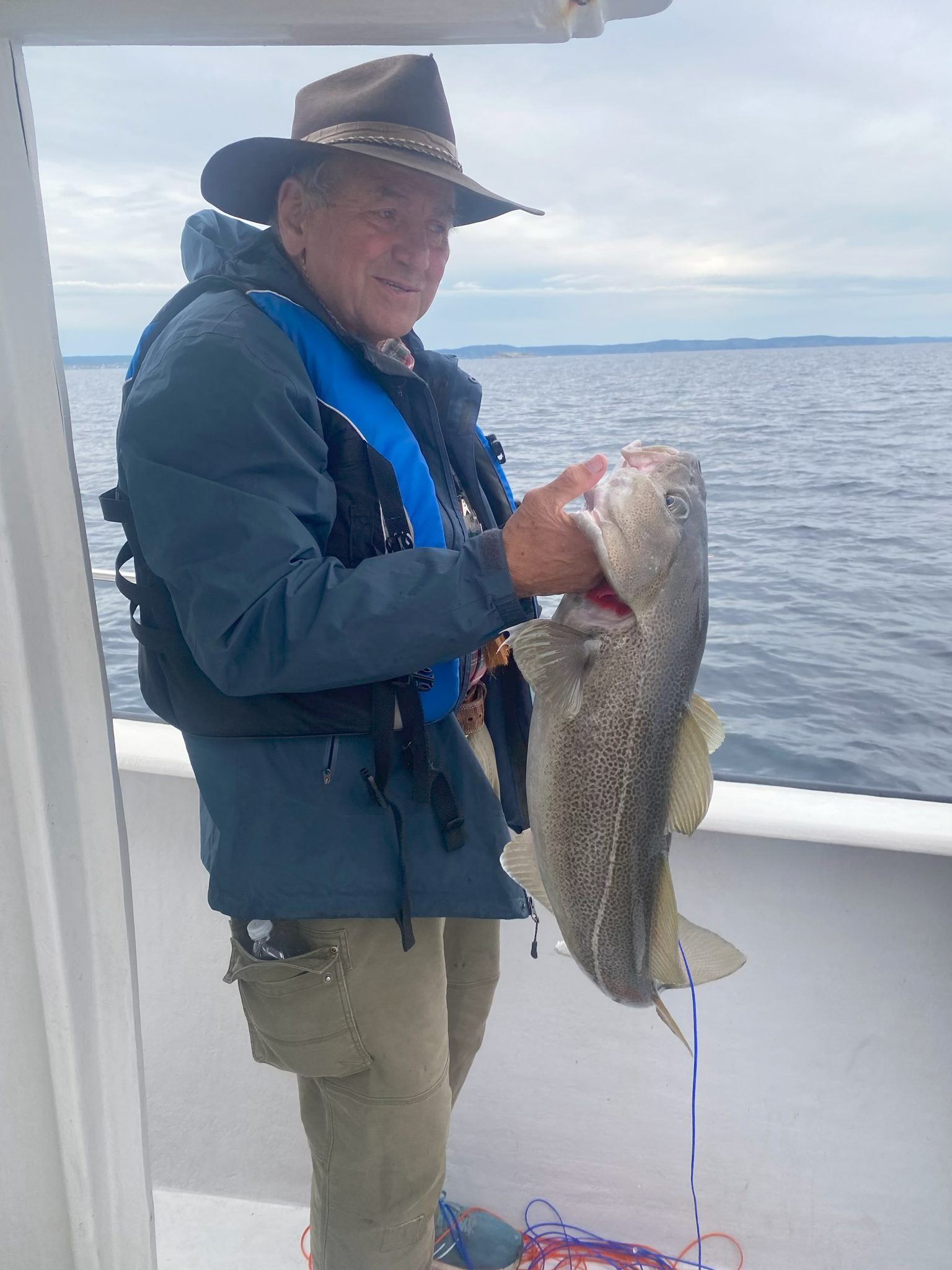 A traveler on a boat holding up a freshly caught cod